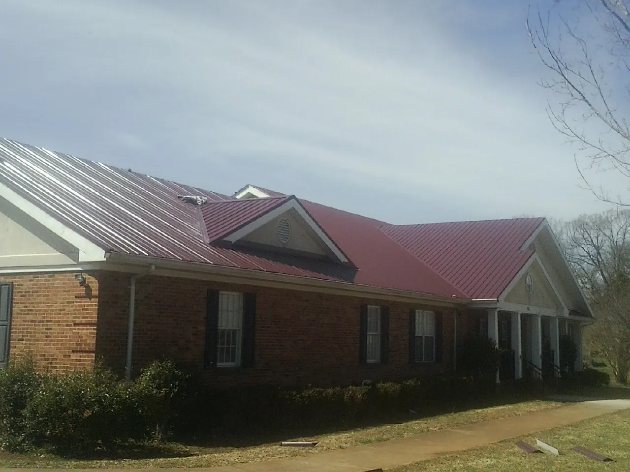Red metal roof with gabled entries on a long brick building, from a Hail Damage Roof Repair job in Lake Helen