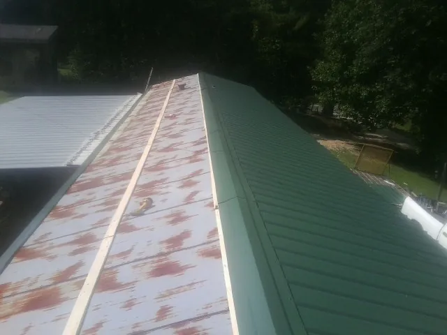 Old rusted panels beside newly installed green metal roofing — Wind Damage Roof Repair by Roofing Brothers in Lake Helen