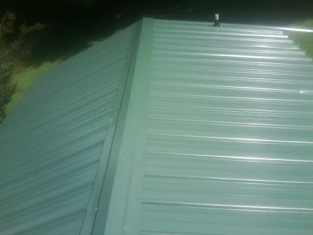 New green metal panels meeting at the ridge of a roof — Flat Roof Repair work by our crew in Lake Helen