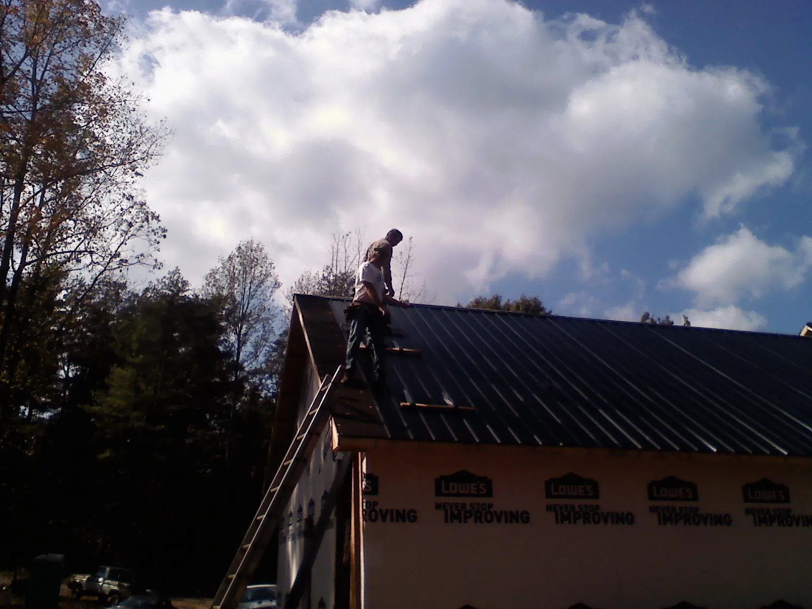Roofer fastening dark metal panels high against a cloudy sky, from a Roof Inspection job in Lake Helen