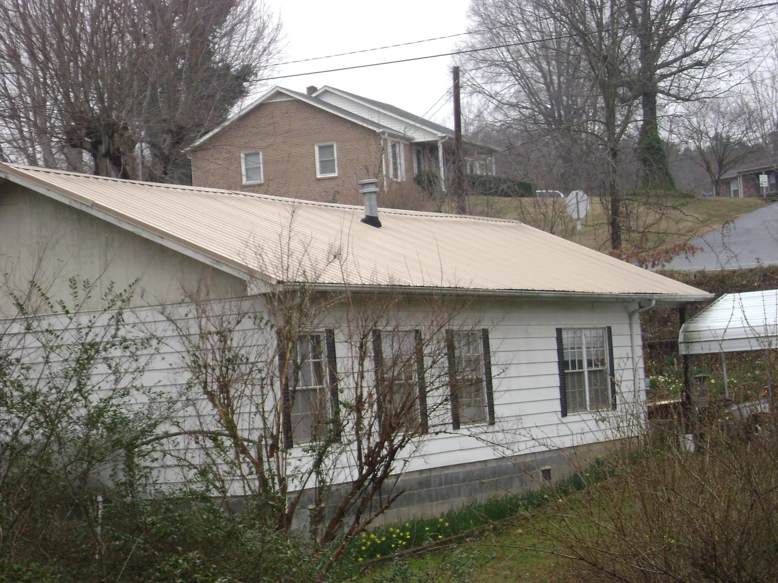 Tan metal roof on a white sided house set into a hillside — Commercial Roofing by Roofing Brothers in Lake Helen